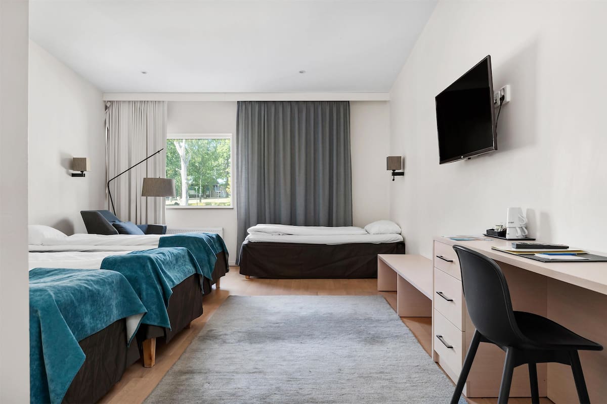 A modern hotel room with two beds, a desk, a chair, a TV, and a window with curtains.