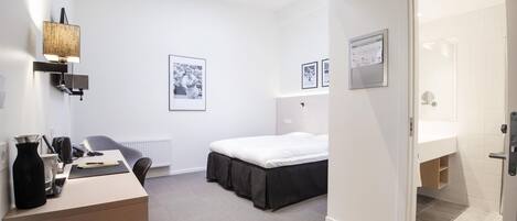 Una habitación de hotel moderna con una cama, un escritorio con lámpara, un radiador y cuadros en la pared.