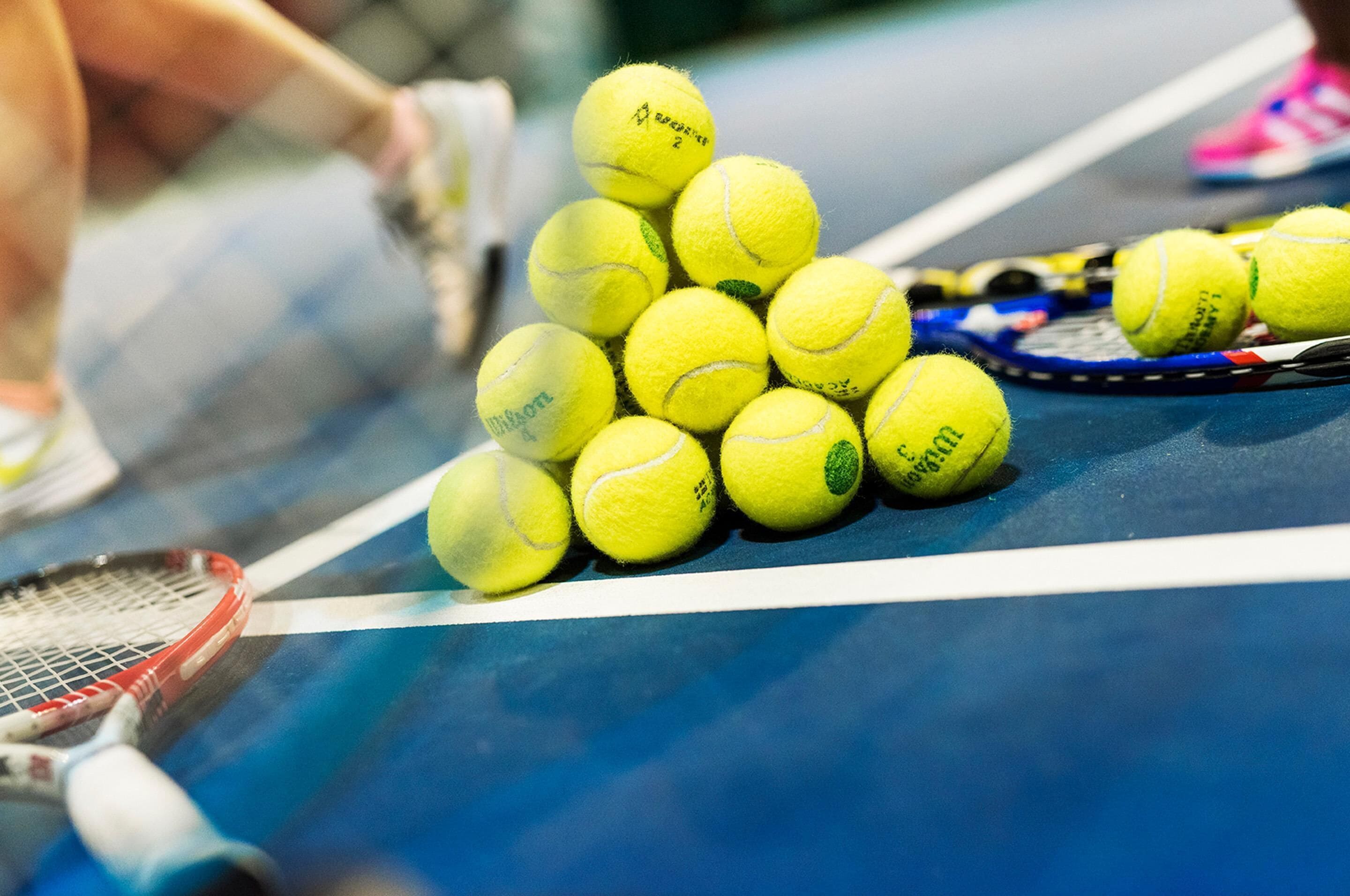 A tennis court with multiple tennis balls and rackets.