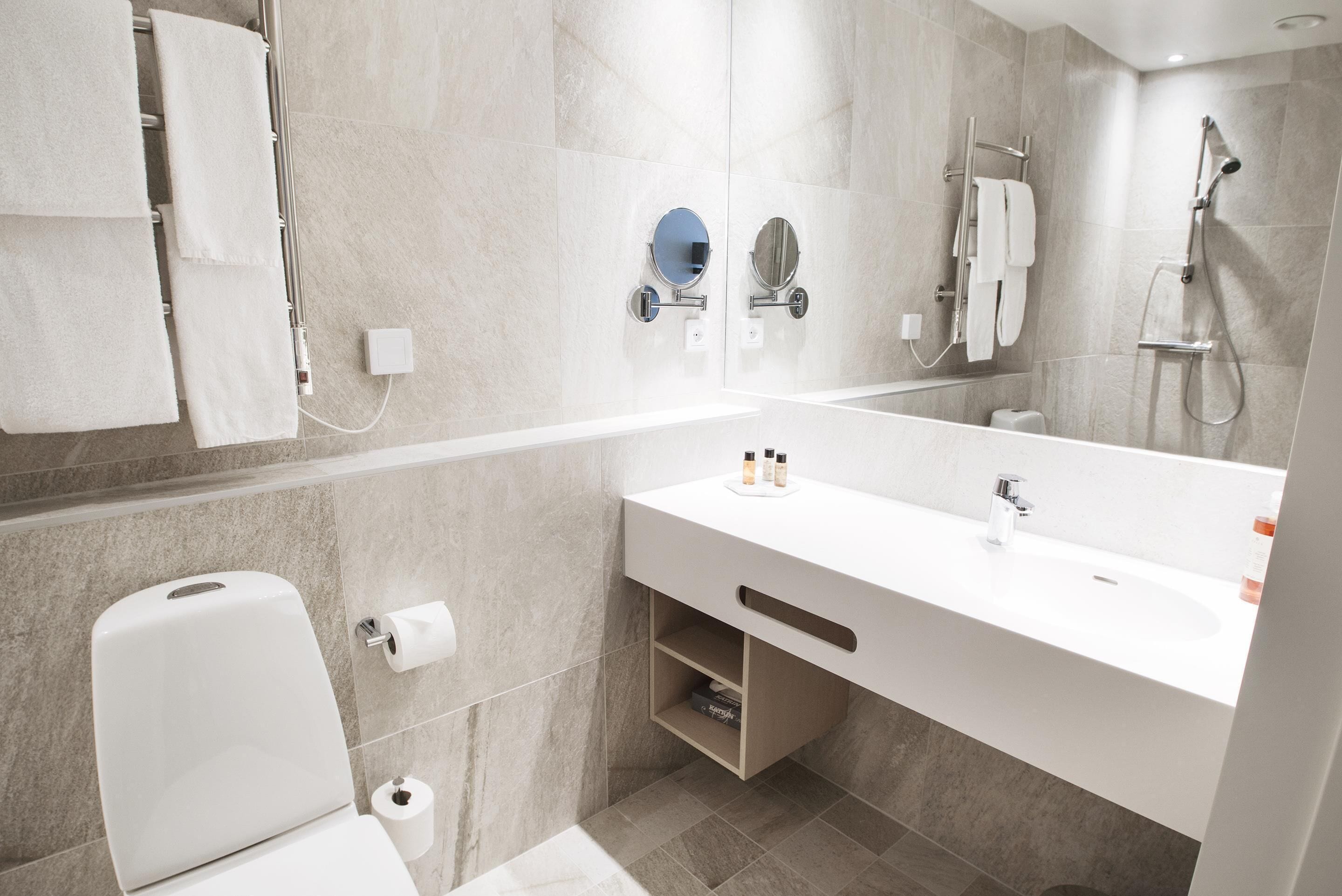 Un baño moderno con lavamanos, espejo y retrete blancos.