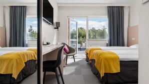 Une chambre d’hôtel avec deux lits, un bureau et une chaise. De grandes fenêtres offrent une vue sur l’extérieur.