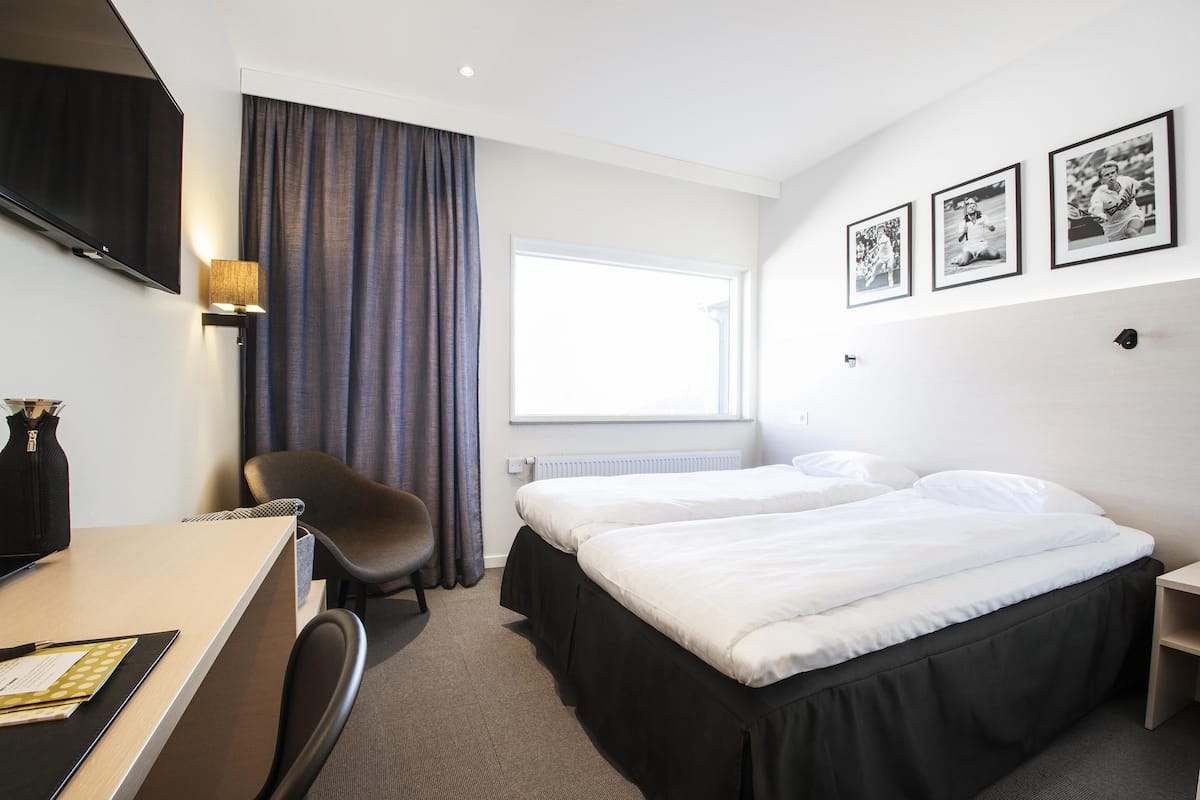 A hotel room with a bed, a desk, a chair, a TV, and a window with curtains.