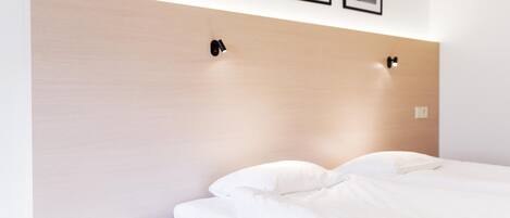 Una cama bien hecha con sábanas blancas, cabecera de madera y dos lámparas fijadas a la pared.