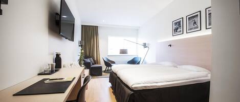 Una habitación de hotel moderna con cama, escritorio, silla, televisión y una obra de arte en la pared.