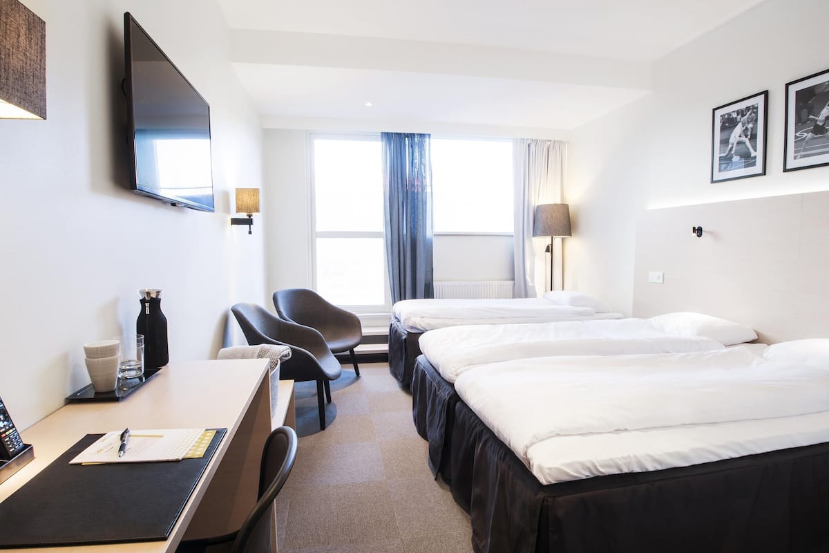 A hotel room with a desk, chair, two beds, a TV, and a window with curtains.