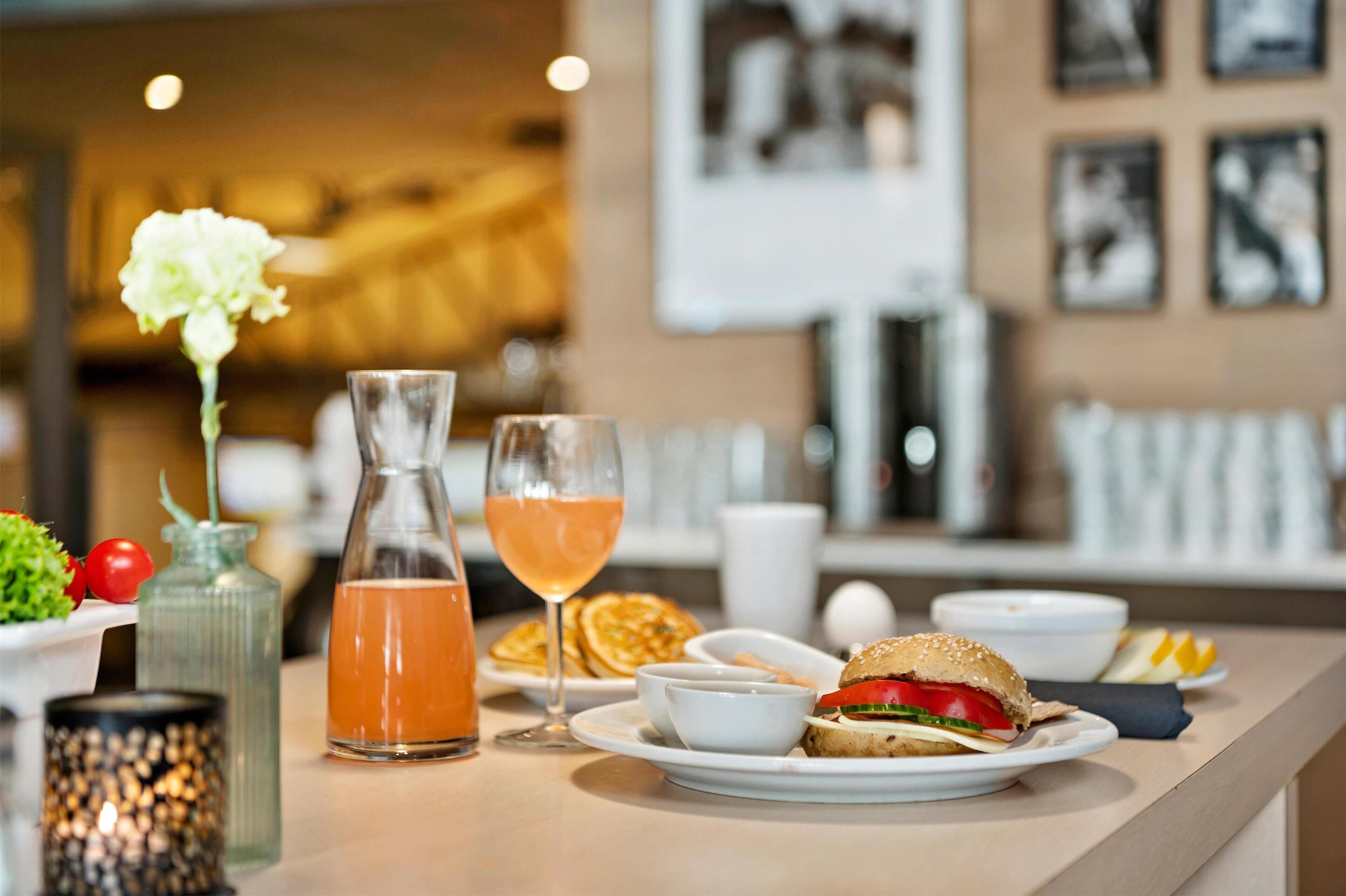 A breakfast setting with a sandwich, a glass of orange juice, and a bottle of water on a table.