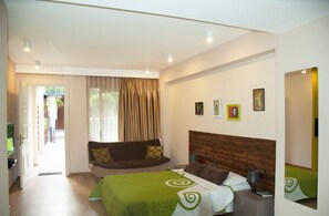 A hotel room with a bed, a sofa, a wooden headboard, and a door leading to a balcony. - Sunrise Arches Apartments (Limassol)
