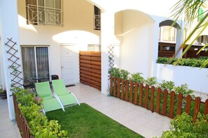 A courtyard with a green lawn, a wooden fence, and a white door. - Sunrise Arches Apartments (Limassol)