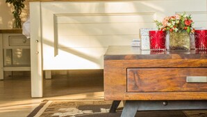 A wooden sideboard with a drawer, a vase with flowers, and two red glassware items. - Motsamai Lodge (Bulawayo)