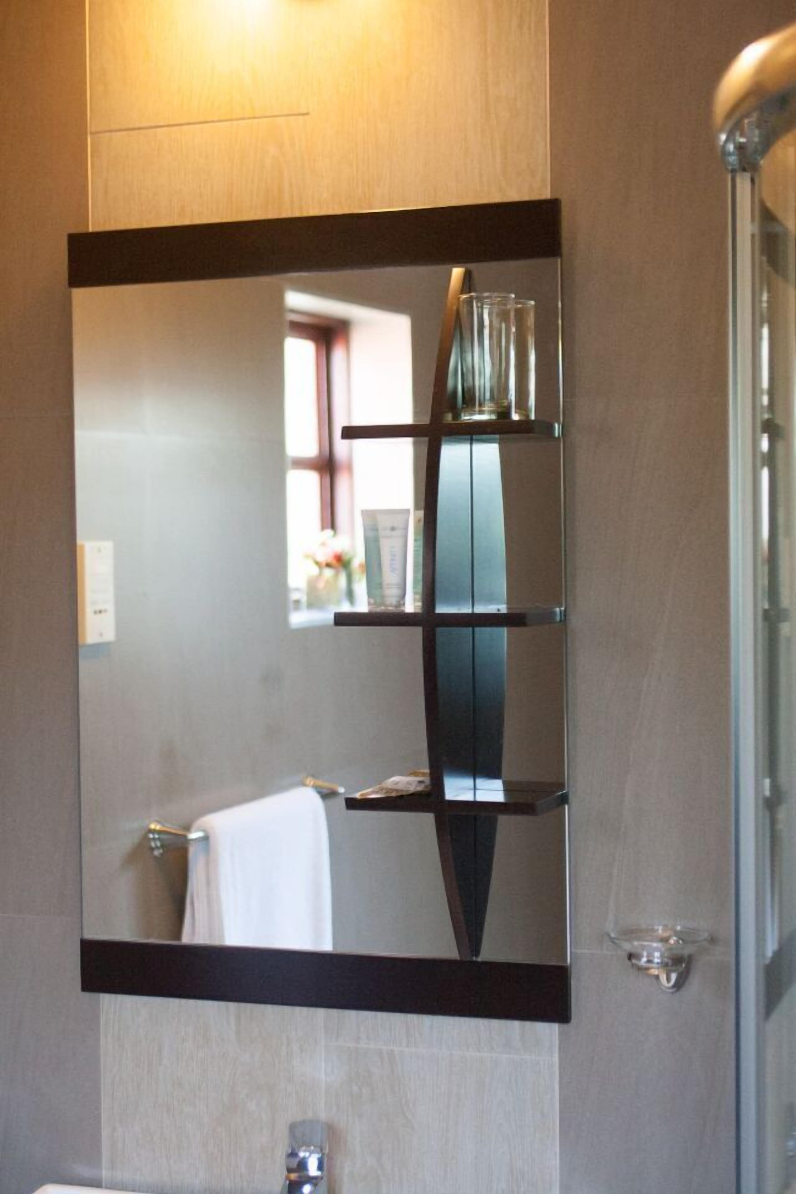 A bathroom with a large mirror, a towel rack, and a glass shelf.