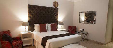 A bedroom with a tufted headboard, a large bed with multiple pillows, two bedside tables with lamps, a red chair, a small table with a mirror, and a bench.