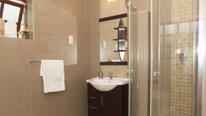 A modern bathroom with a glass shower enclosure, a white sink, and a dark vanity. - Motsamai Lodge (Bulawayo)