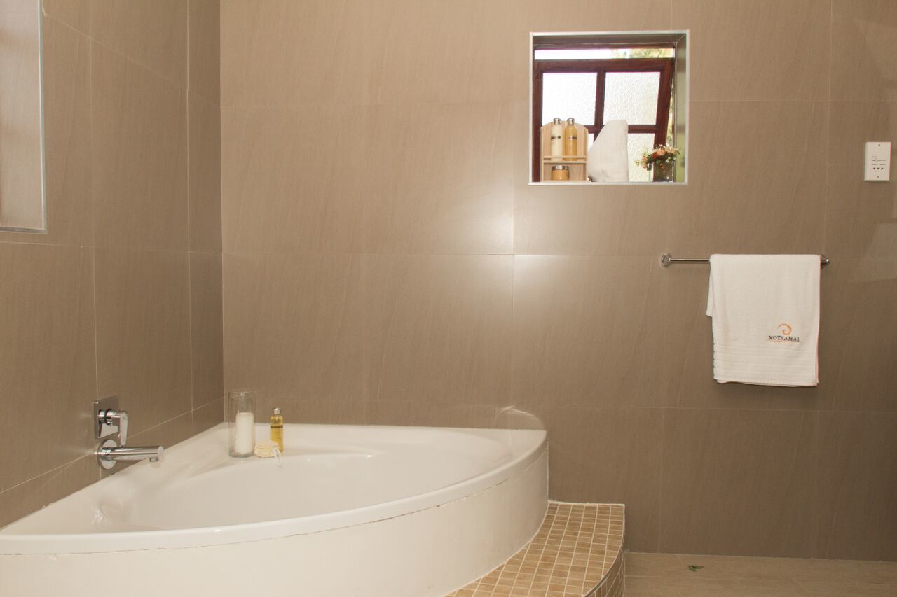 Un baño con una bañera grande, un perchero con una toalla y un espejo que refleja una ventana con botellas en un estante.