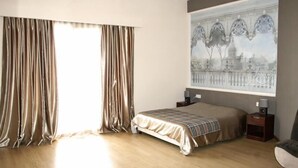 A bedroom with a bed, curtains, a nightstand, a lamp, and a painting on the wall. - Sunrise Studios (Limassol)