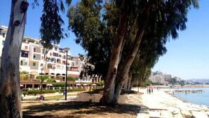 A coastal promenade with a row of multi-story buildings, a sandy beach, and a clear blue sky. - Sunrise Studios (Limassol)