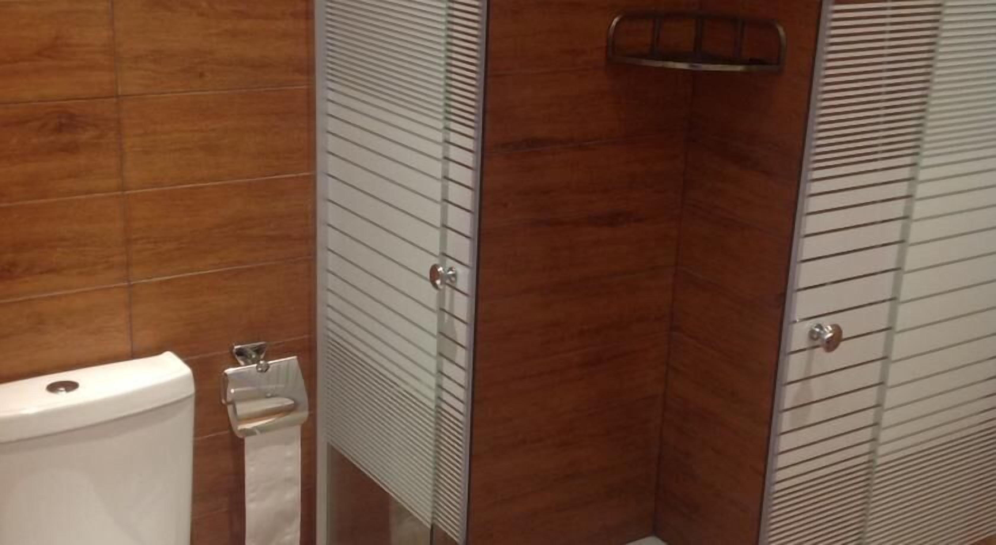 Et badeværelse med toilet, håndklædeautomat og en brusekabine med glasdør.
