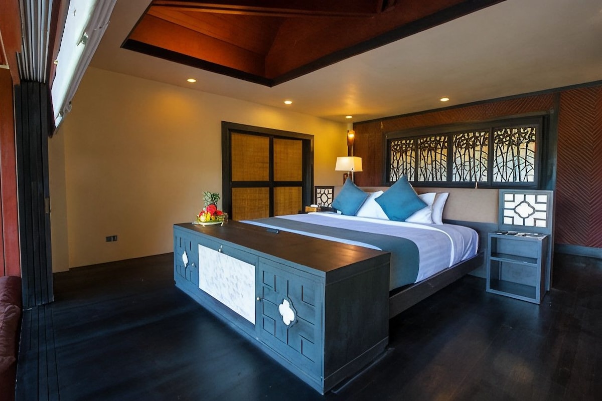 A bedroom with a large bed, a bedside table, a nightstand, and a decorative wall panel.