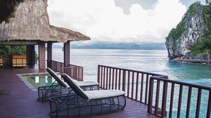 A deck with lounge chairs and a pool, overlooking a body of water and a mountainous landscape. - Cauayan Boutique Private Island (El Nido)