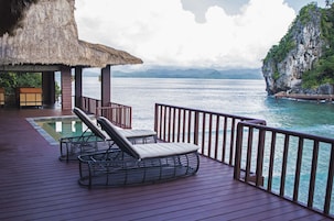 Terraço com espreguiçadeiras e piscina, com vista para um corpo de água e uma paisagem montanhosa.