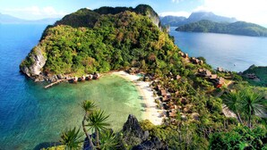 A tropical island with a beach, clear waters, and lush greenery. - Cauayan Boutique Private Island (El Nido)