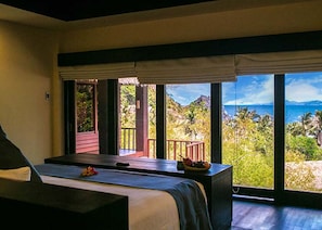 A room with a bed, a massage table, and a view of the ocean and hills. - Cauayan Boutique Private Island (El Nido)