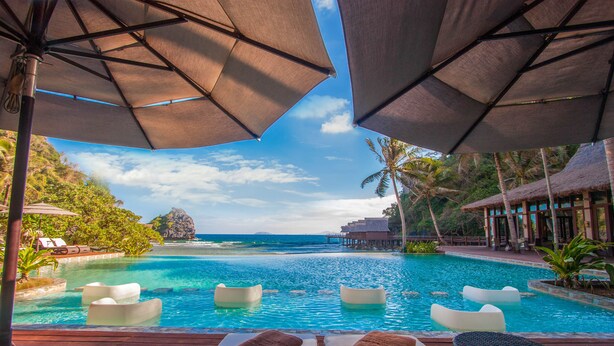 A poolside area with lounge chairs and umbrellas, overlooking a clear blue pool and ocean view. - Cauayan Boutique Private Island (El Nido)