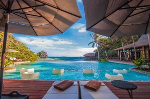 Área da piscina com espreguiçadeiras e guarda-sóis, com vista para uma piscina azul e o oceano.