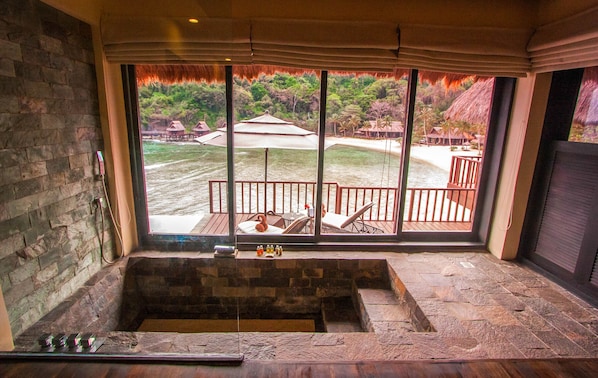 A stone bathtub with a view of a deck and beach. - Cauayan Boutique Private Island (El Nido)