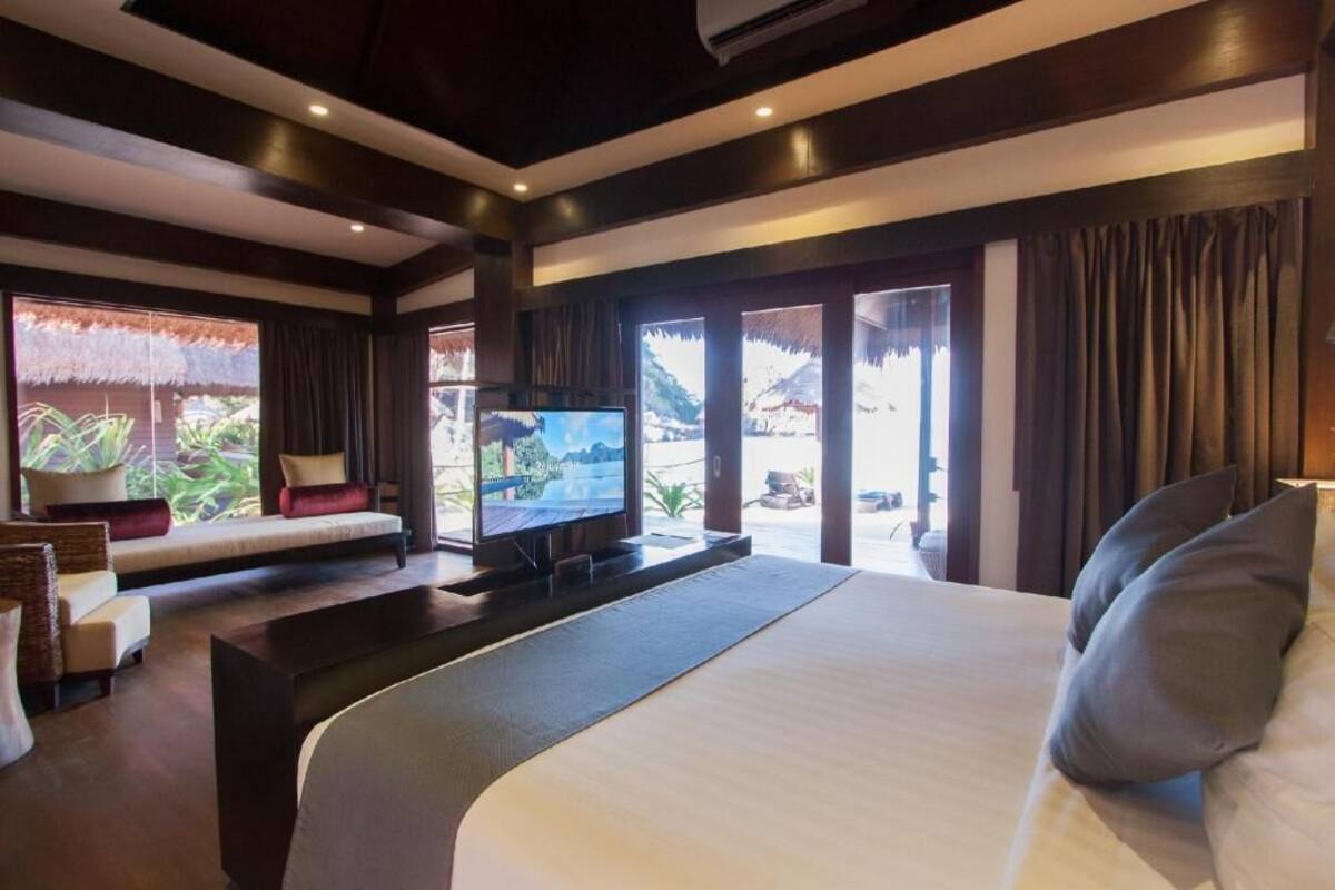 Ein modernes Hotelzimmer mit einem großen Bett, einem Flachbildfernseher, einer Sitzecke mit Kissen und Blick ins Freie.