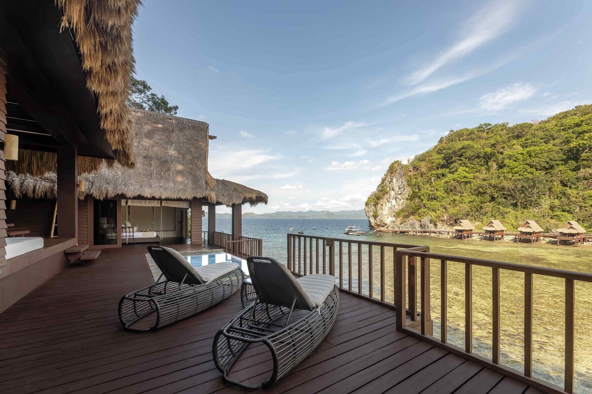 A wooden deck with lounge chairs overlooking a beach and ocean.