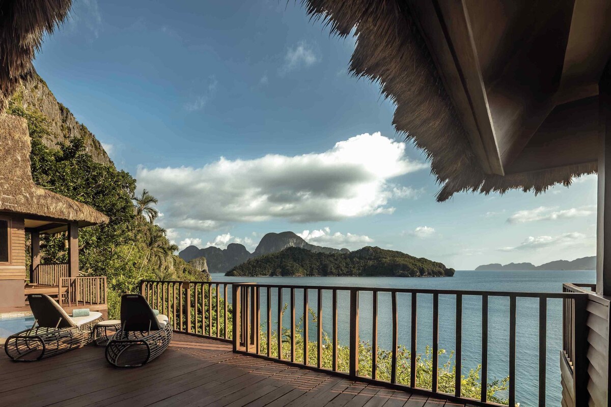 A wooden deck with lounge chairs overlooking a body of water and distant mountains.