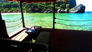 A wooden deck with a table and benches overlooking a clear turquoise sea, with thatched roof and rope barriers. - Cauayan Boutique Private Island (El Nido)