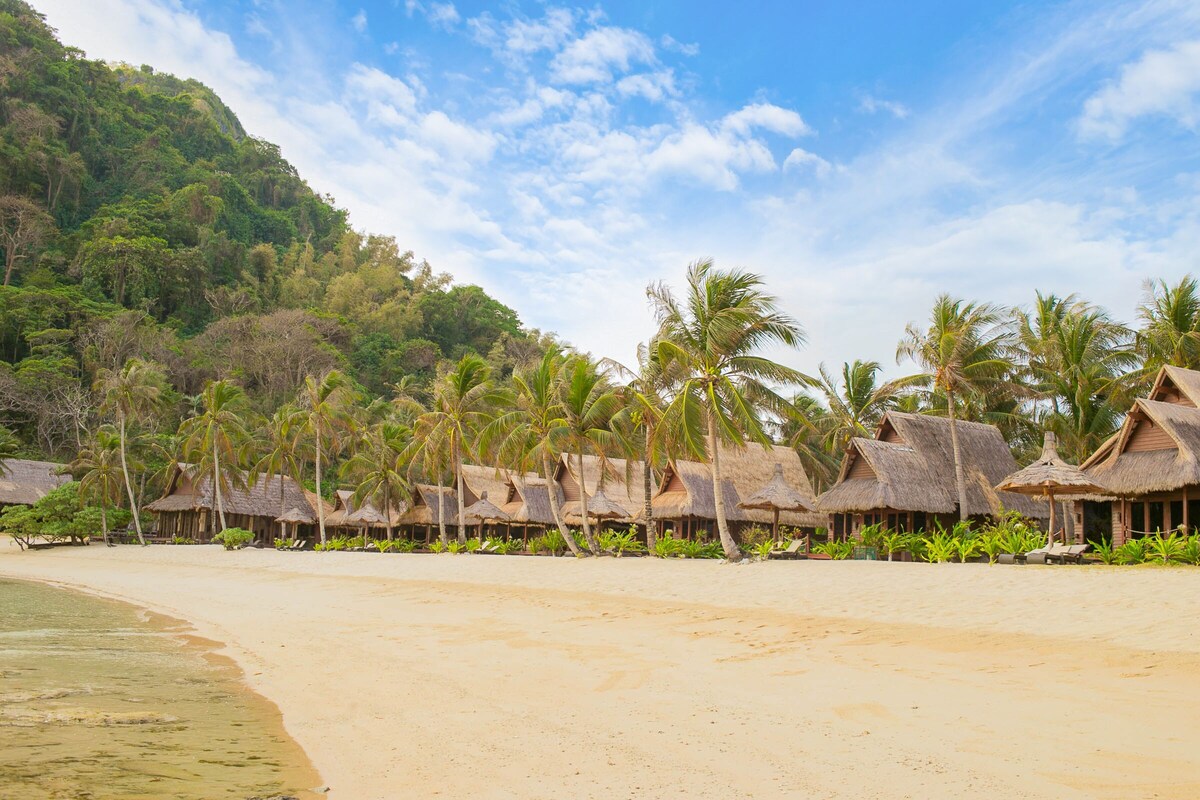 A beach with thatched-roof huts and palm trees.