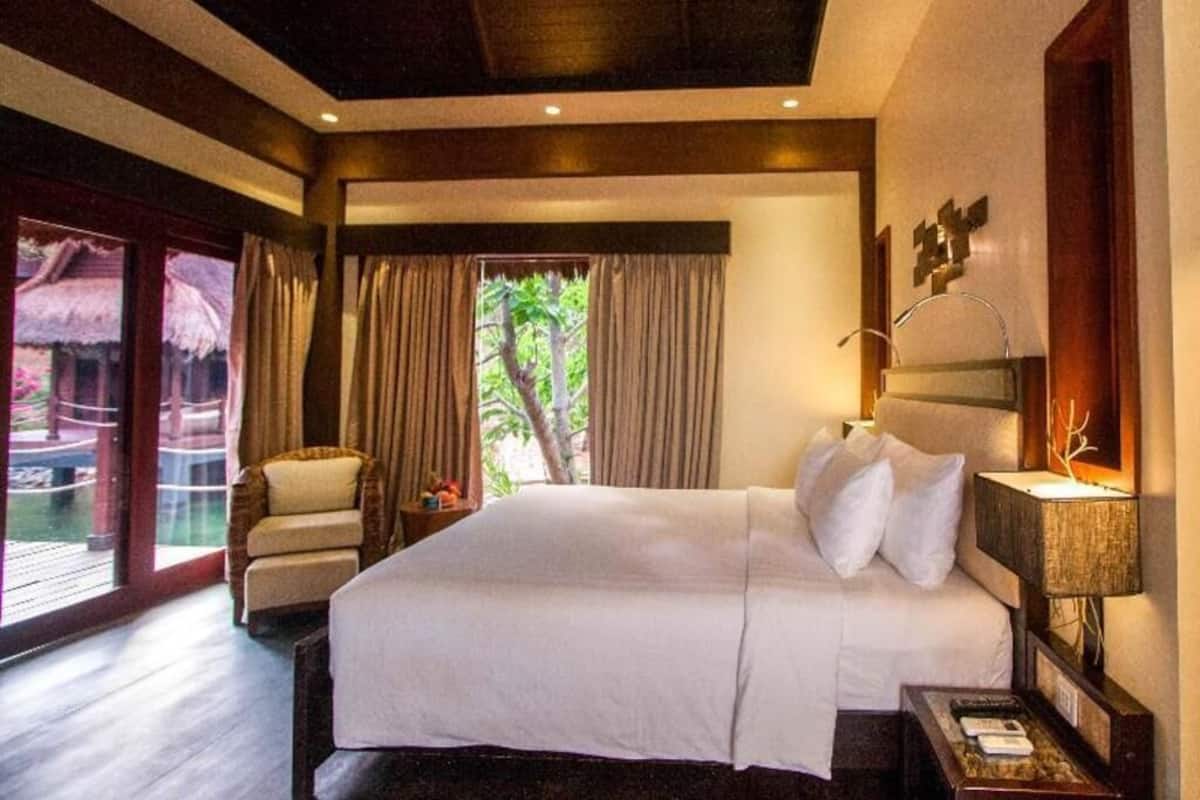 Ein Hotelzimmer mit Bett, Stuhl, Nachttisch und Blick ins Freie.