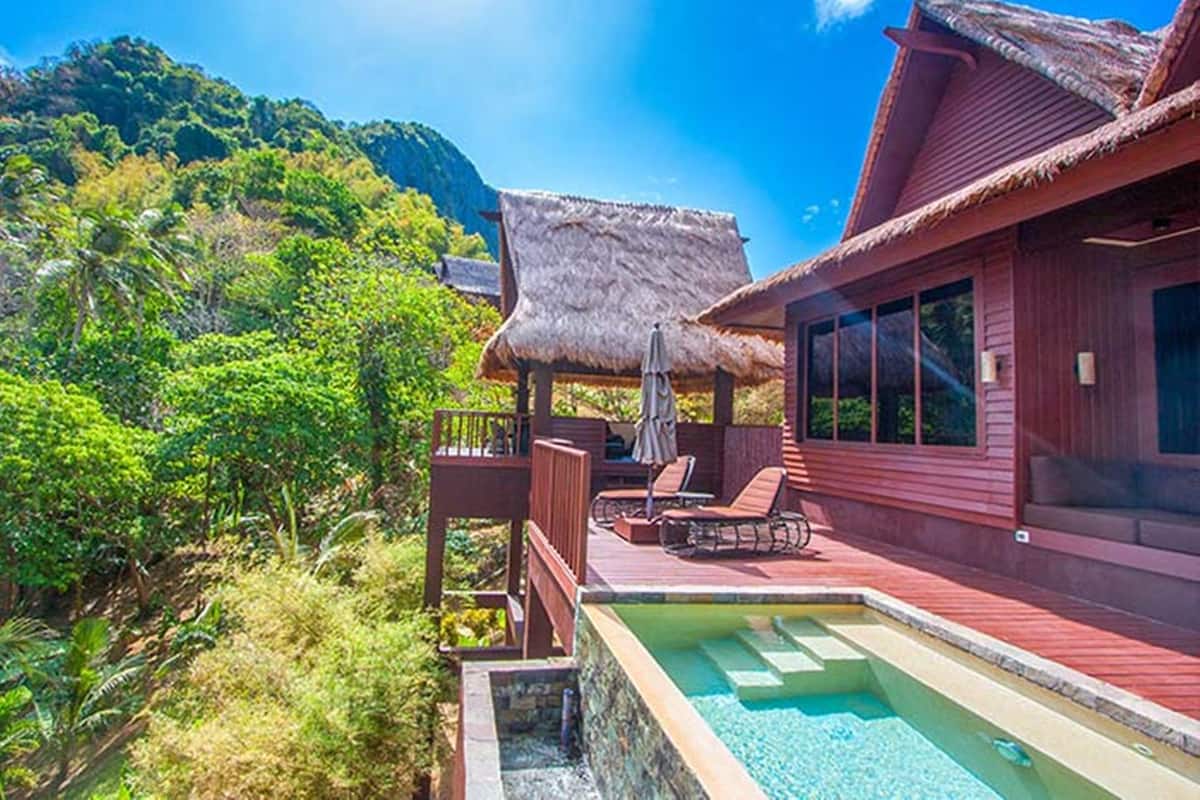 Eine Holzvilla mit Pool, einem Gebäude mit Strohdach und üppigem Grün.