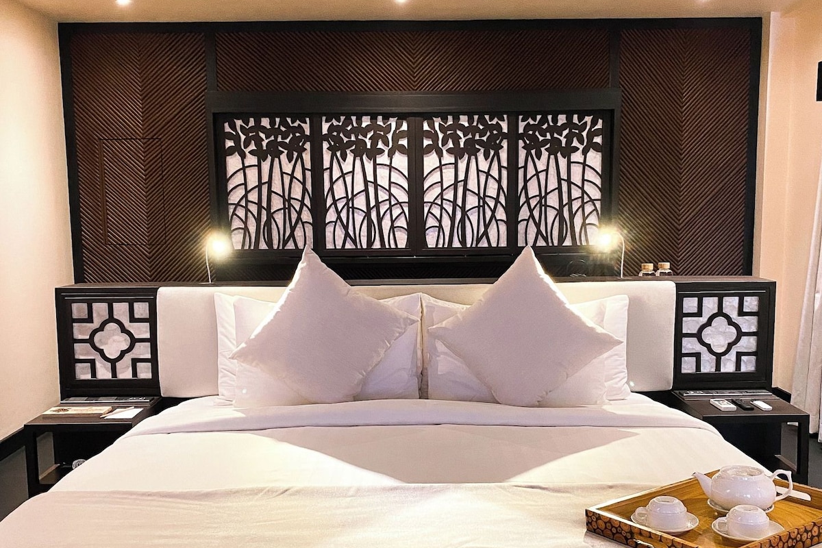 A hotel room with a large bed, two bedside tables, a decorative headboard, and a tray with tea set.
