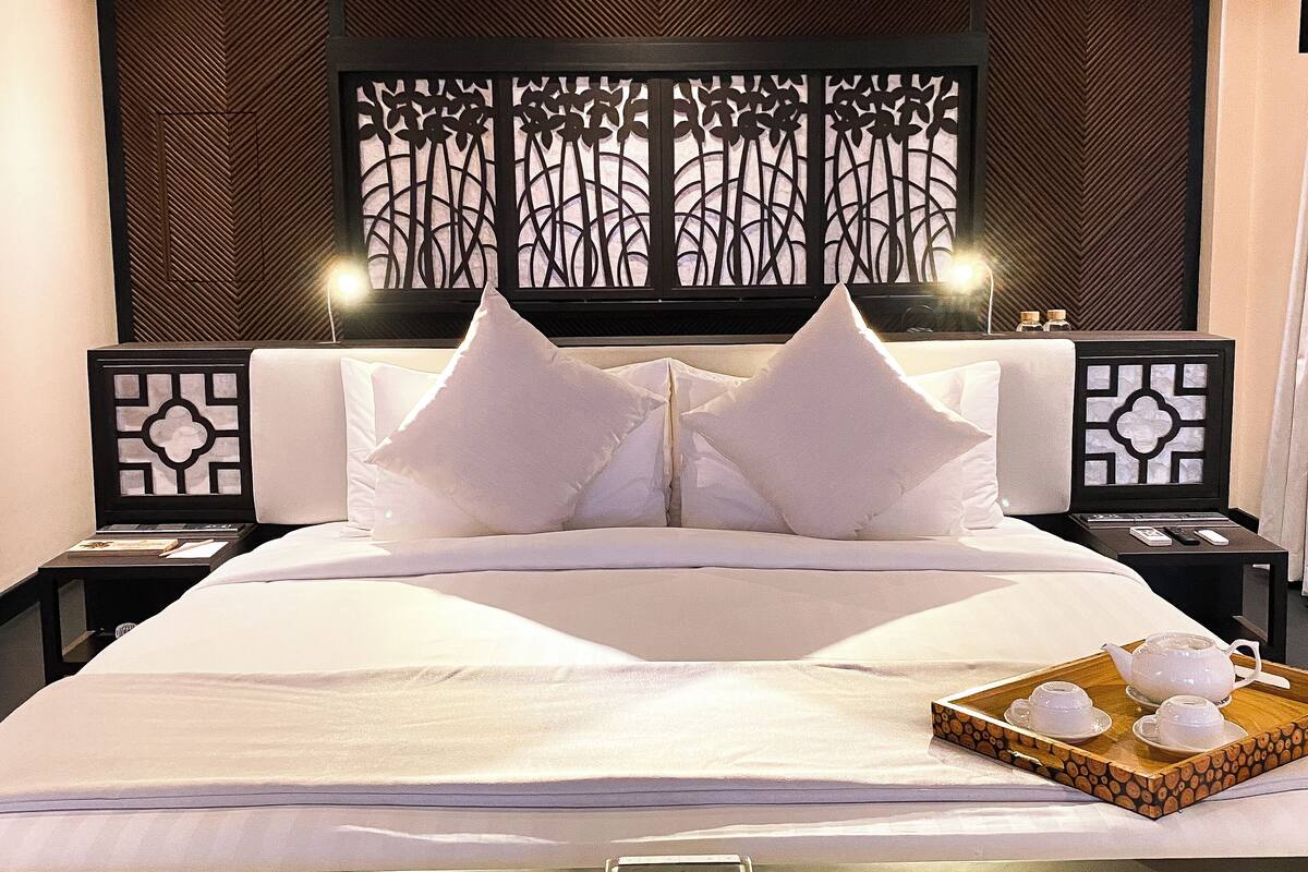Ein Hotelzimmer mit einem großen Bett, zwei Nachttischen, einem dekorativen Kopfteil und einer Ablage mit Teetassen und einem Teekessel.