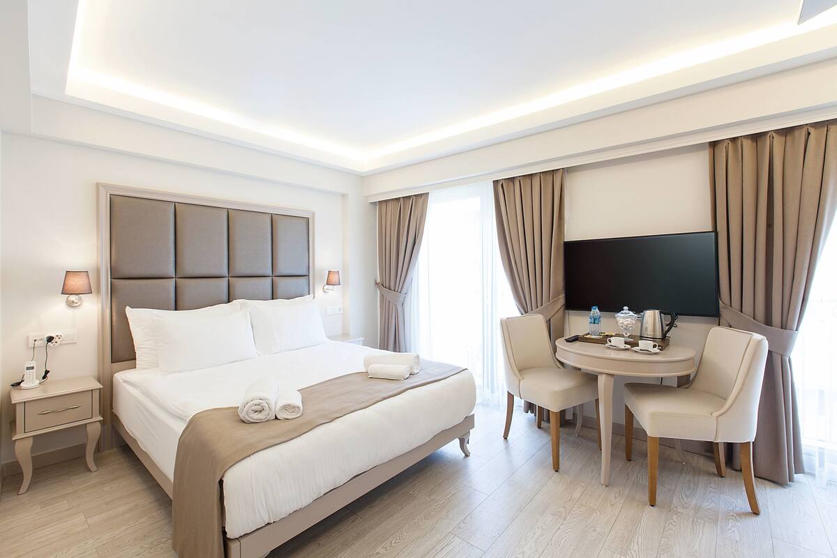 Une chambre d’hôtel avec un grand lit, des tables de chevet, un bureau avec des chaises, un téléviseur à écran plat et des rideaux.