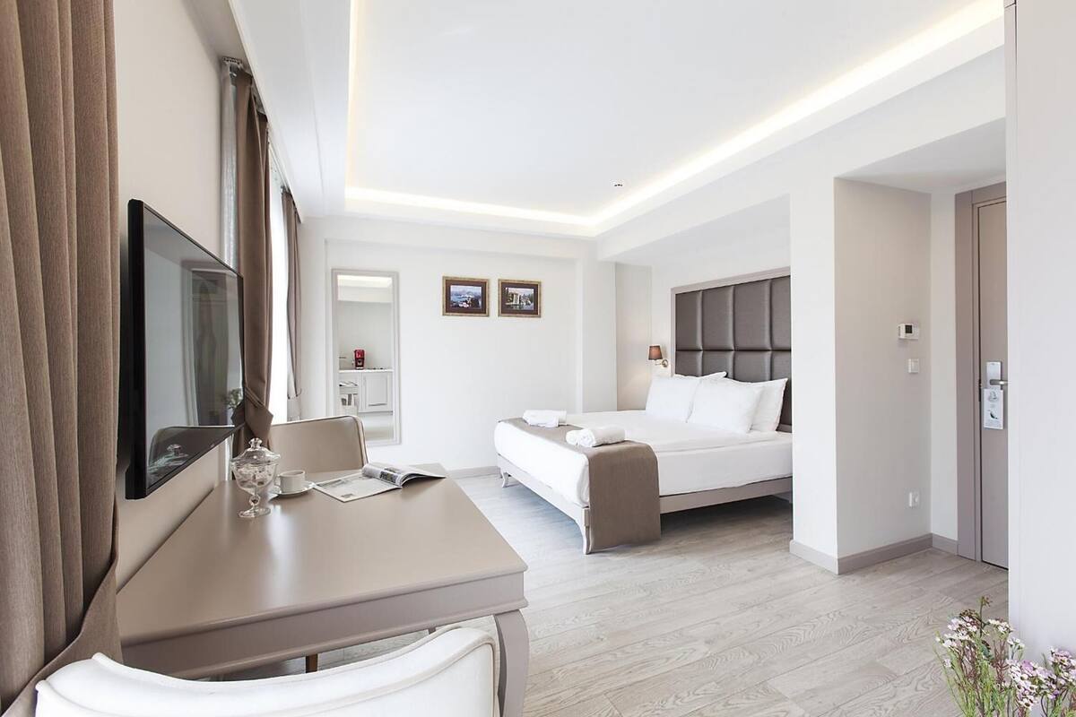 Une chambre d’hôtel moderne équipée d’un lit, d’un bureau avec une chaise, d’une télévision et d’une petite table avec un verre.
