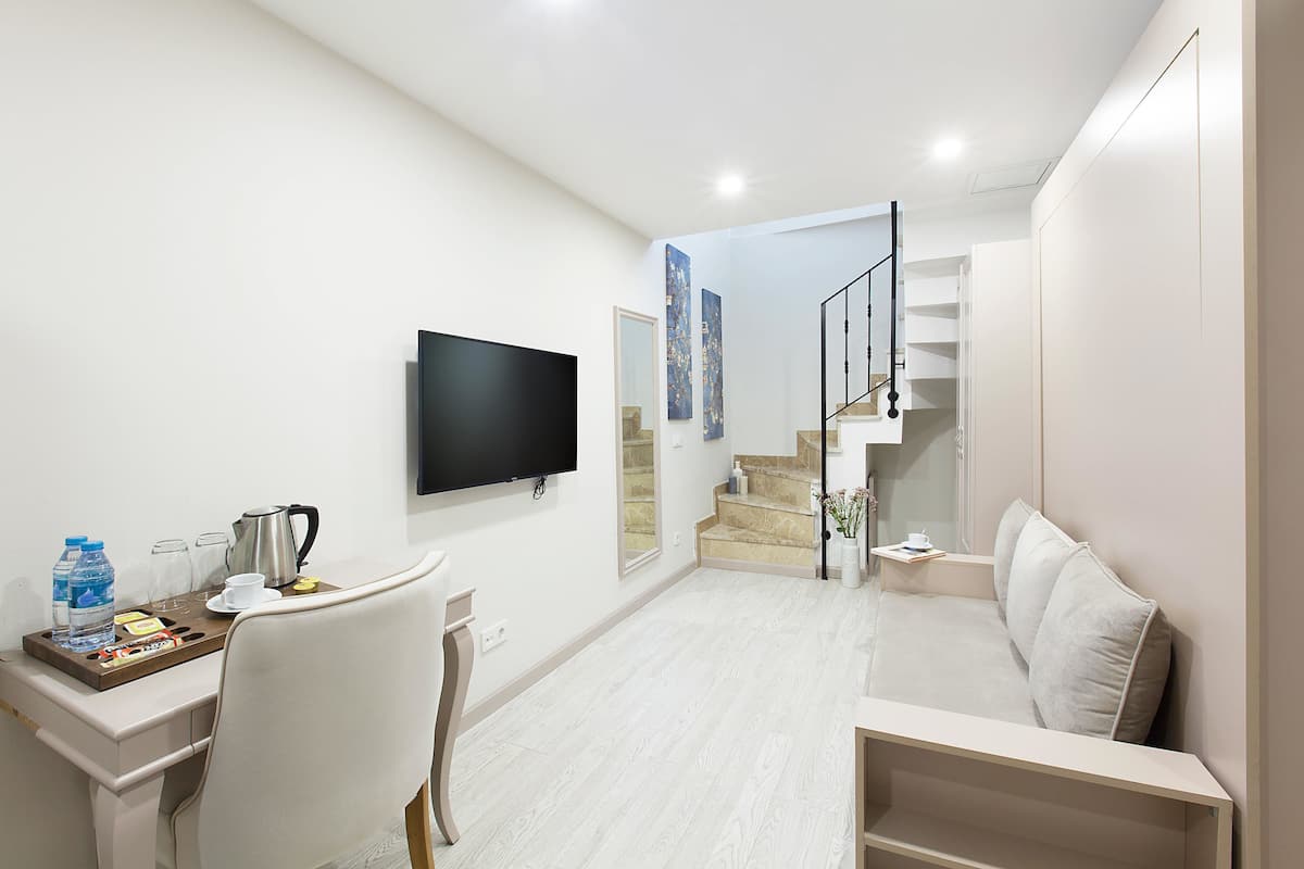 Une chambre d’hôtel moderne dotée d’une télévision à écran plat, d’un bureau avec des articles pour le petit-déjeuner, d’un canapé et d’un escalier menant à l’étage supérieur.