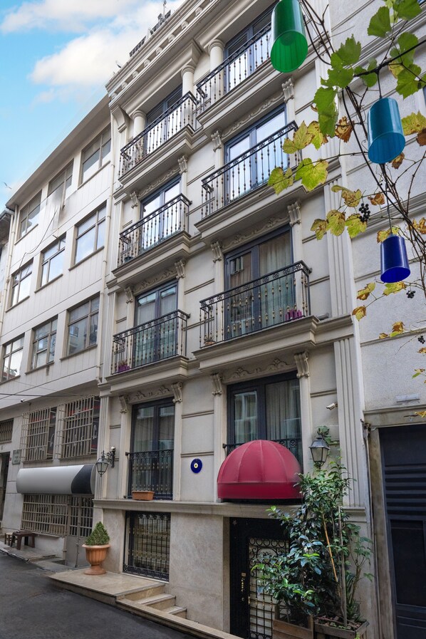 Un edificio de varios pisos con balcones, un toldo rojo y plantas en macetas.