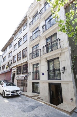 Un edificio de varios pisos con balcones, un coche estacionado y un letrero de comercio.