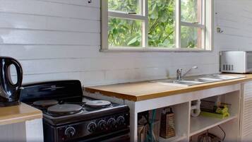 Una cocina equipada con estufa, microondas, hervidor y pileta.