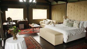 Une chambre spacieuse avec un grand lit, un canapé, une petite table et un bureau. Deux fenêtres laissent entrer la lumière naturelle.