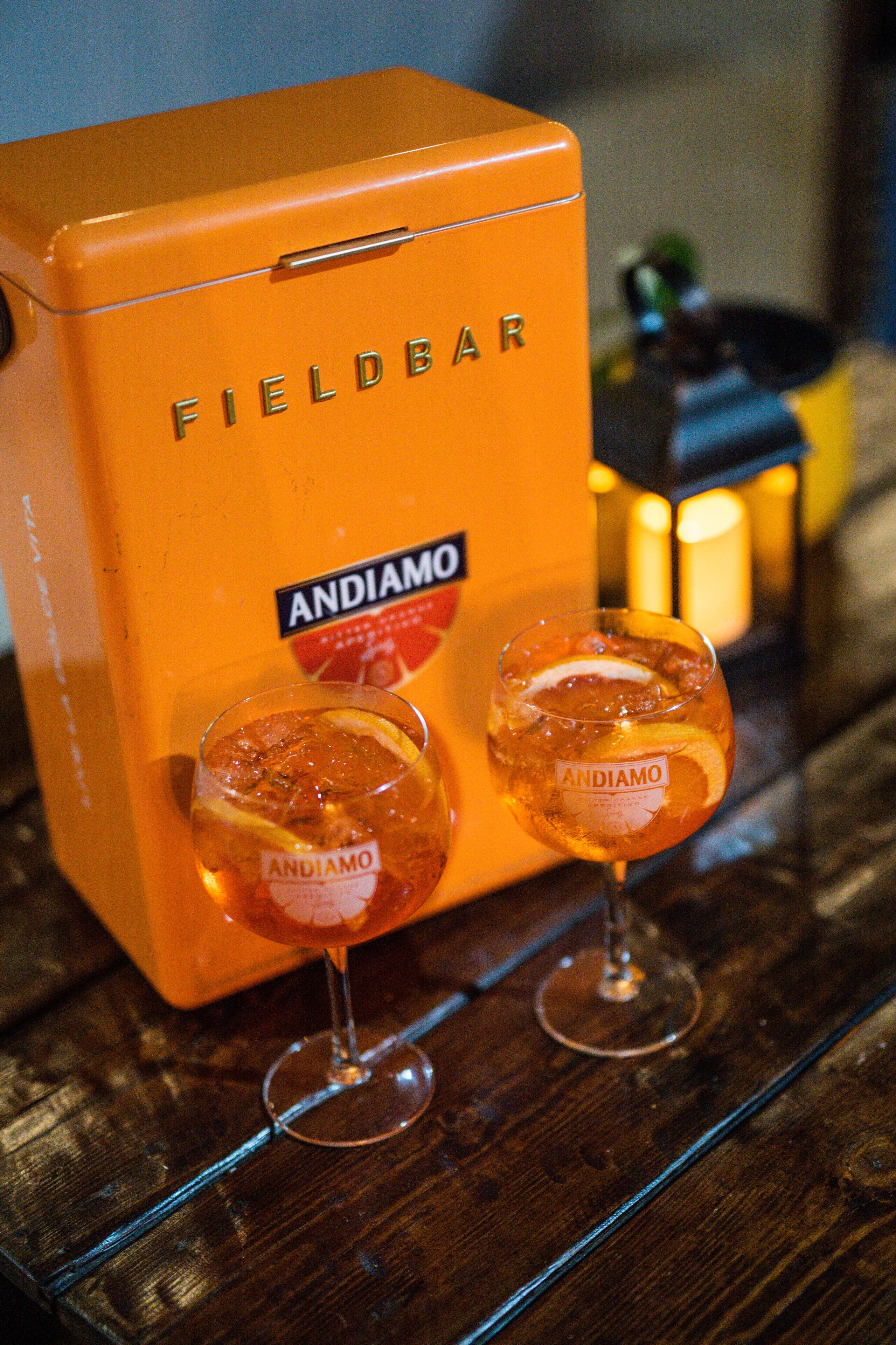 Una caja naranja FIELDBAR con dos copas de vino ANDIAMO.