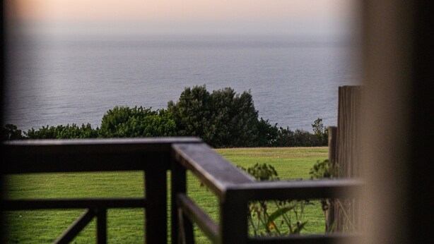Une vue depuis un balcon donnant sur une zone herbeuse, avec une balustrade en bois et un plan d’eau visible au loin.