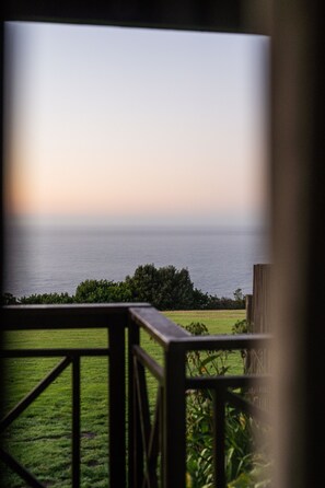 A view from a balcony overlooking a grassy area with a wooden railing and a distant body of water.