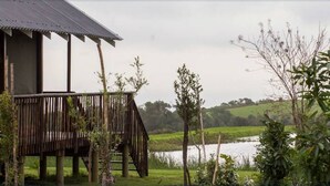 Une construction rustique en bois, dotée d’un balcon donnant sur une étendue d’eau et sur des collines verdoyantes en arrière-plan.