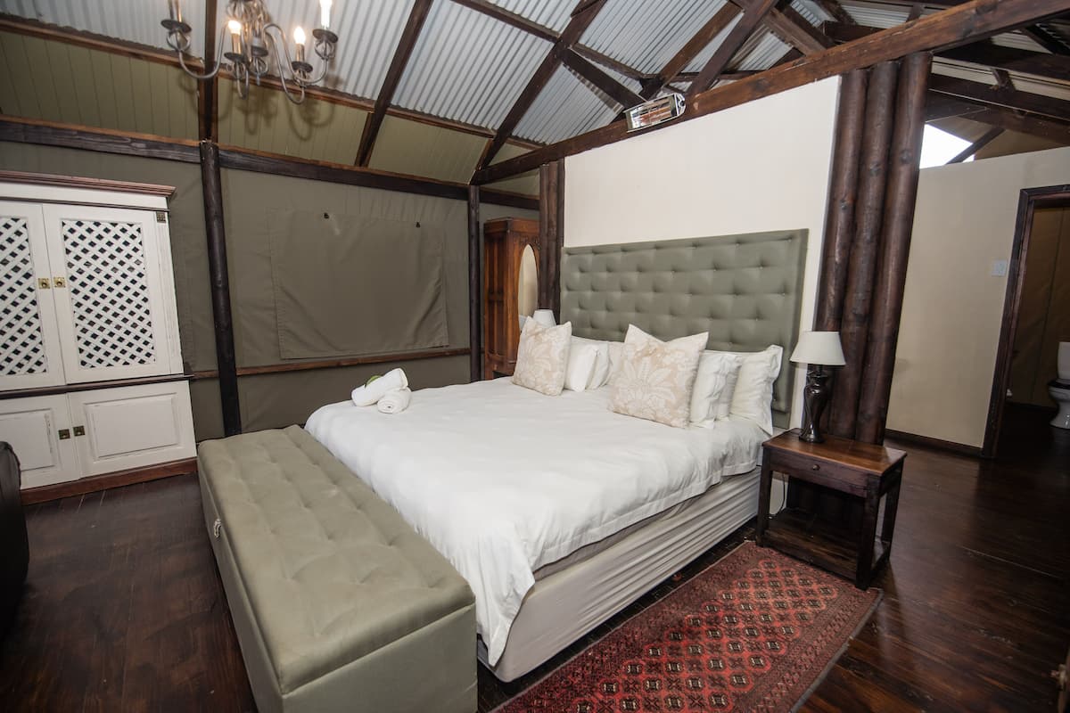 A spacious bedroom with a large bed, a bench, a wooden headboard, a nightstand, and a chandelier.