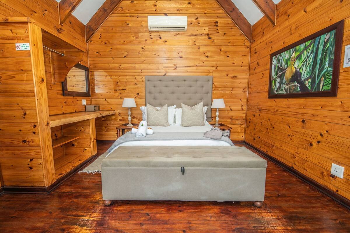 A log cabin-style bedroom with a large bed, two bedside tables, a headboard, and a painting on the wall.